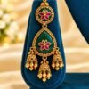 Emerald-green meena jhumka earring on a teal stand, side light