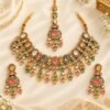 Pastel stone necklace set with maang tikka and earrings laid flat on ivory fabric